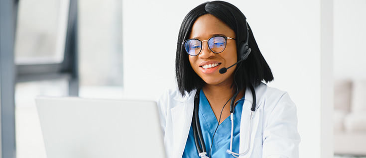 A pair of hands typing on a laptop with the screen showing a telemedicine video call with doctors.